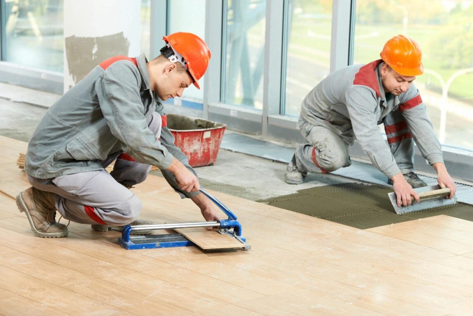 Two men in construction hats are working on a floor.